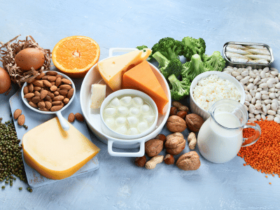 Calciumreiche Lebensmittel wie Käse, Gemüse und Nüsse auf blauem Tisch.