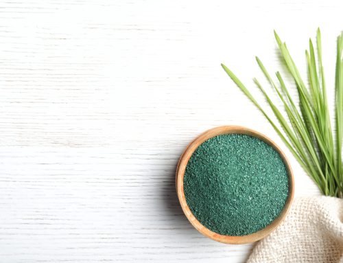Spirulinapulver in einer Schale, daneben hat es Gras